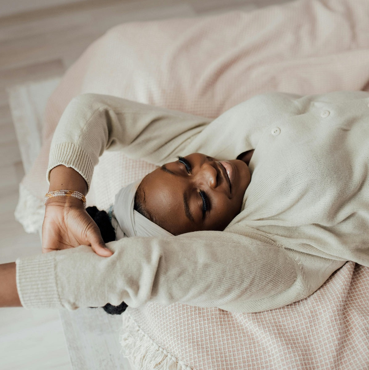 A woman lies on a bed with her eyes closed and arms stretched out, looking relaxed and peaceful.