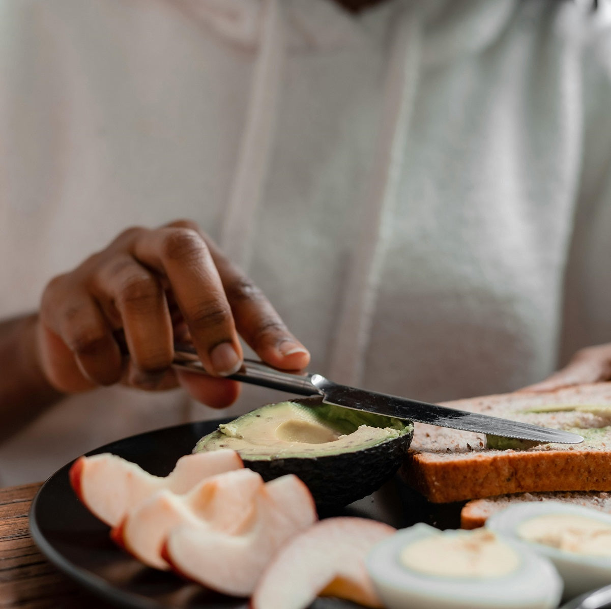 Close-up of a man spreading avocado on whole-grain toast alongside boiled eggs and apple slices.